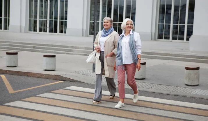 Dve nasmejane starije žene lagano prelaze ulicu u udobnoj obući