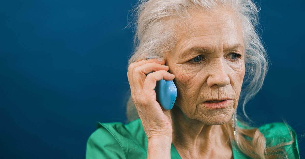 Starija žena drži telefon uz uvo i napregnuto sluša sagovornika